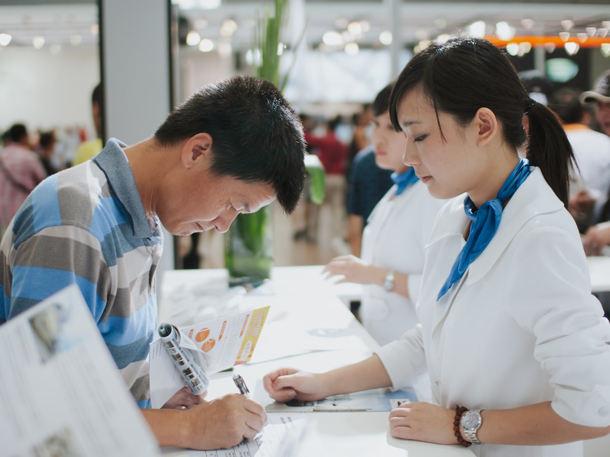 A staff member helping a visitor fill out and sign a document at a service counter