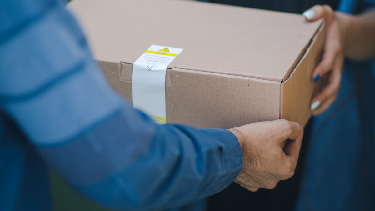 Two people handing over a taped cardboard box outdoors, the kind of in-person handoff at the heart of a Danggeun trade.