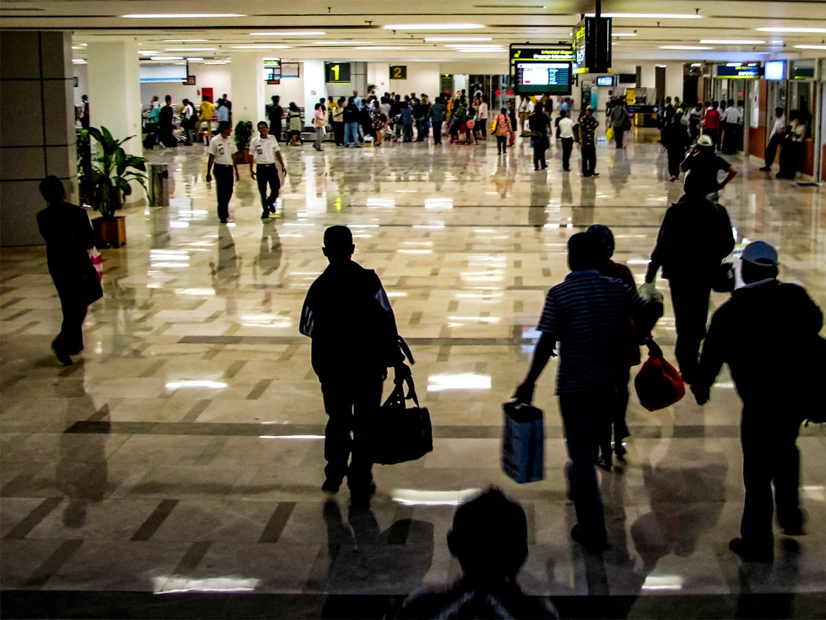 Travelers walking through a large airport terminal hall carrying luggage