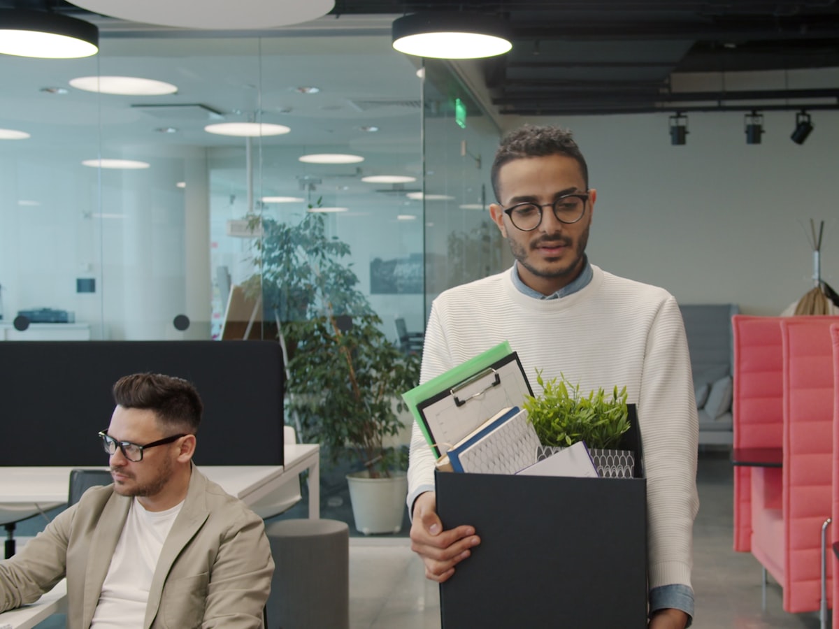 A man carrying a box of personal belongings out of a modern office