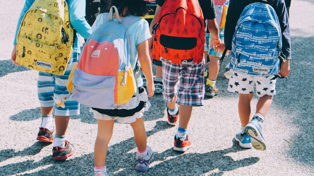 A group of elementary school children with colorful backpacks walking together outdoors on a sunny day.