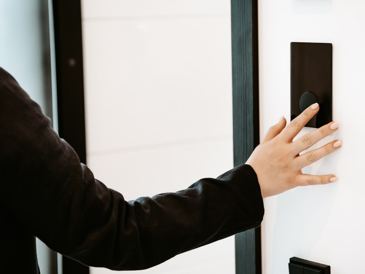 A hand reaching to press a modern black digital door lock panel mounted beside a light-colored apartment door