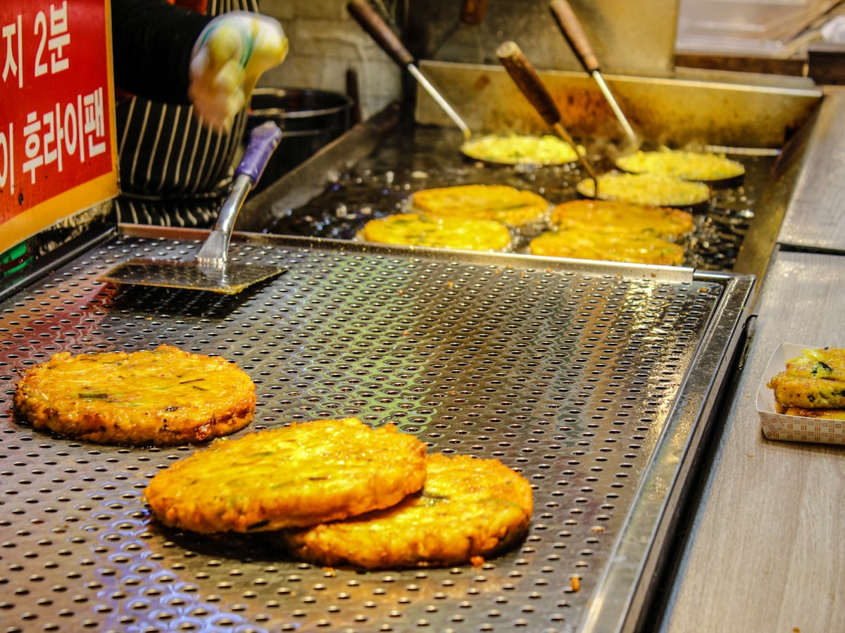Savory Korean jeon pancakes sizzling on an oiled market griddle, the rainy-day comfort food traditionally paired with makgeolli.