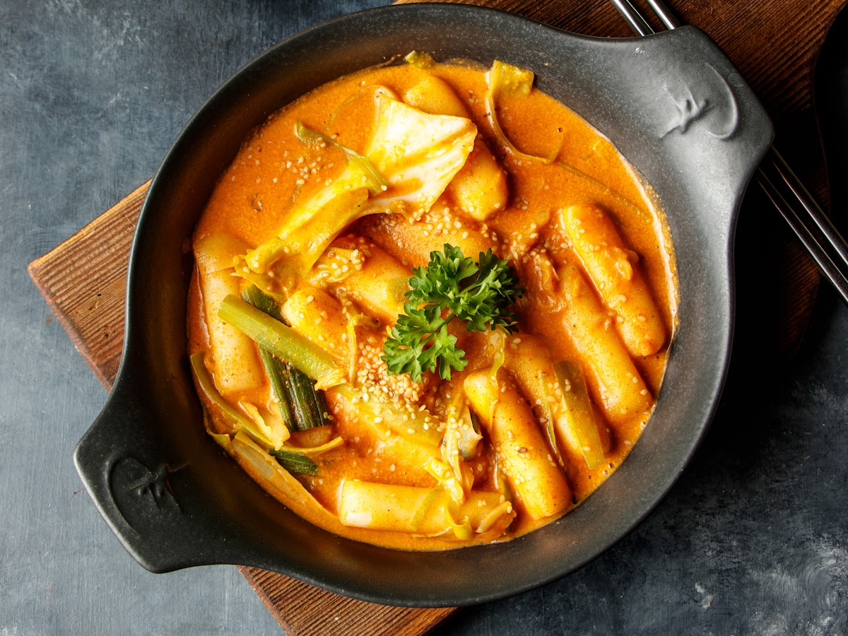 A bowl of spicy tteokbokki served with kimchi and pickled radish banchan at a modern Korean table setting