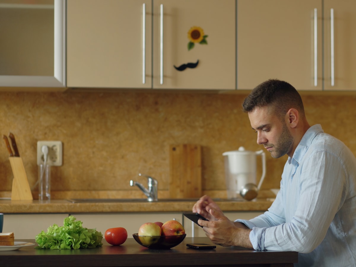 A man checking his phone with a serious expression at a kitchen table in the morning