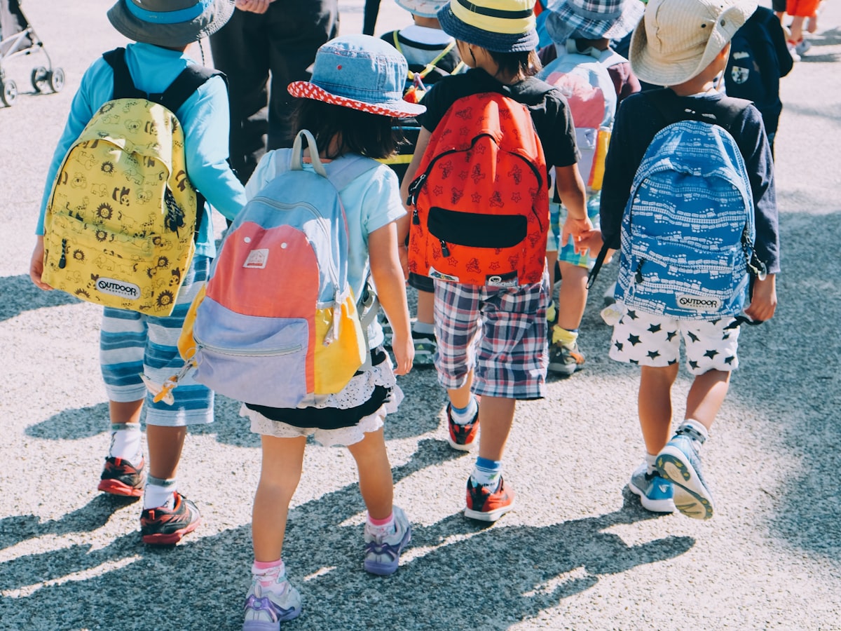 A group of elementary school children in colorful backpacks and sun hats walking together on a school outing