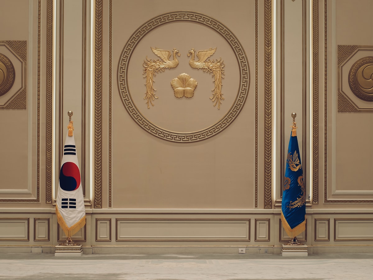 Two Korean flags — the Taegukgi and the presidential standard — flanking a gilded phoenix emblem in a formal reception room at Cheong Wa Dae, Seoul's former presidential residence