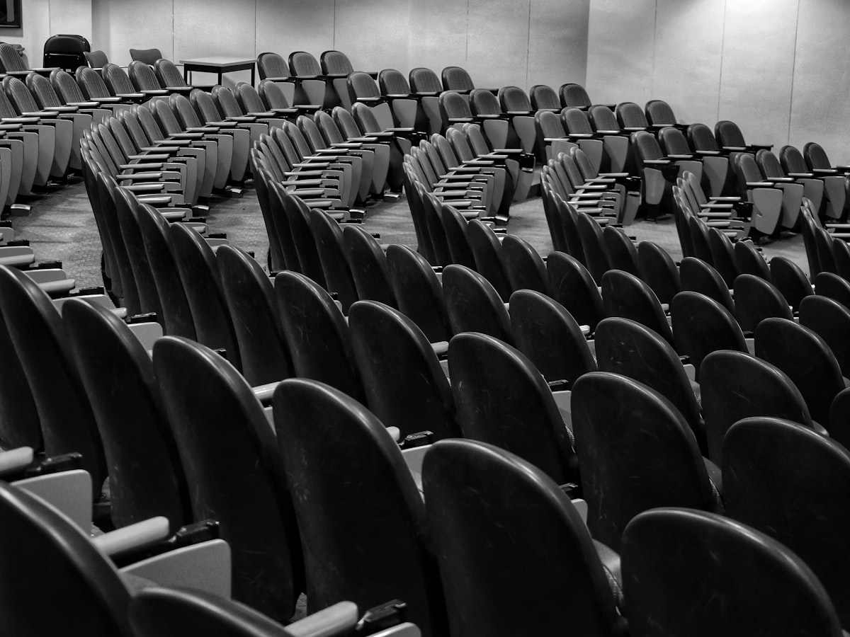 Rows of empty chairs in a quiet, dimly lit hall, black and white