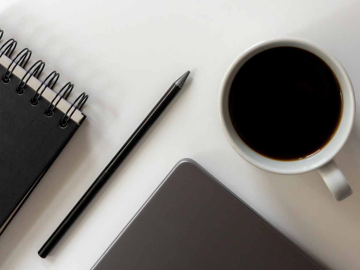 A notebook, pen, phone, and a cup of coffee laid out on a desk, evoking the routine of sitting down with lease and insurance paperwork
