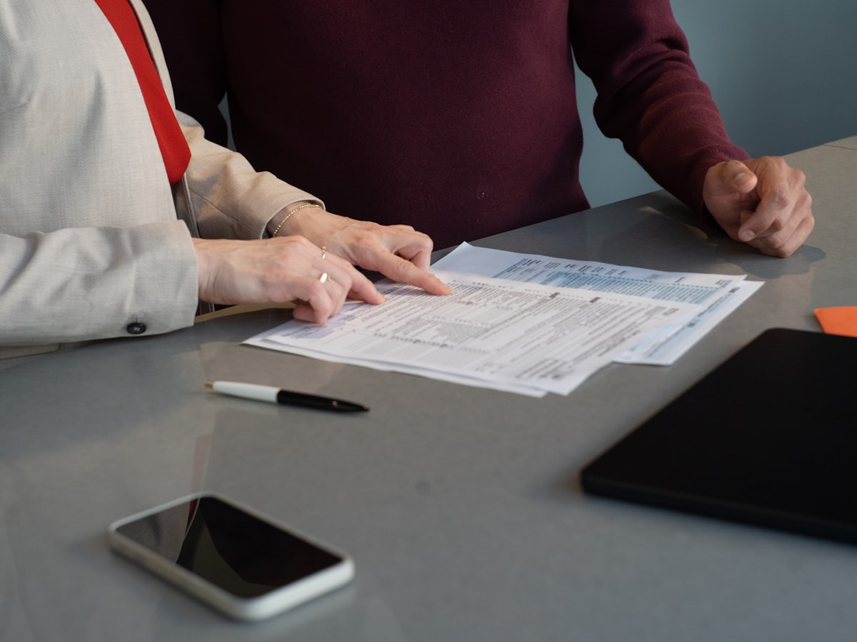 Two people reviewing a printed form on a table, with a phone and tablet nearby