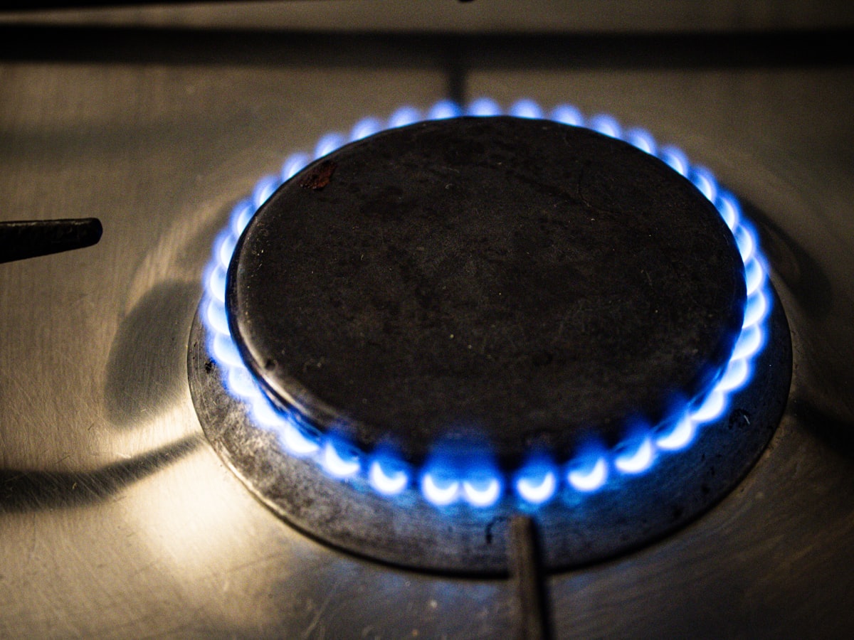 Close-up of a blue gas flame ringing a stovetop burner during a leak and open-flame check