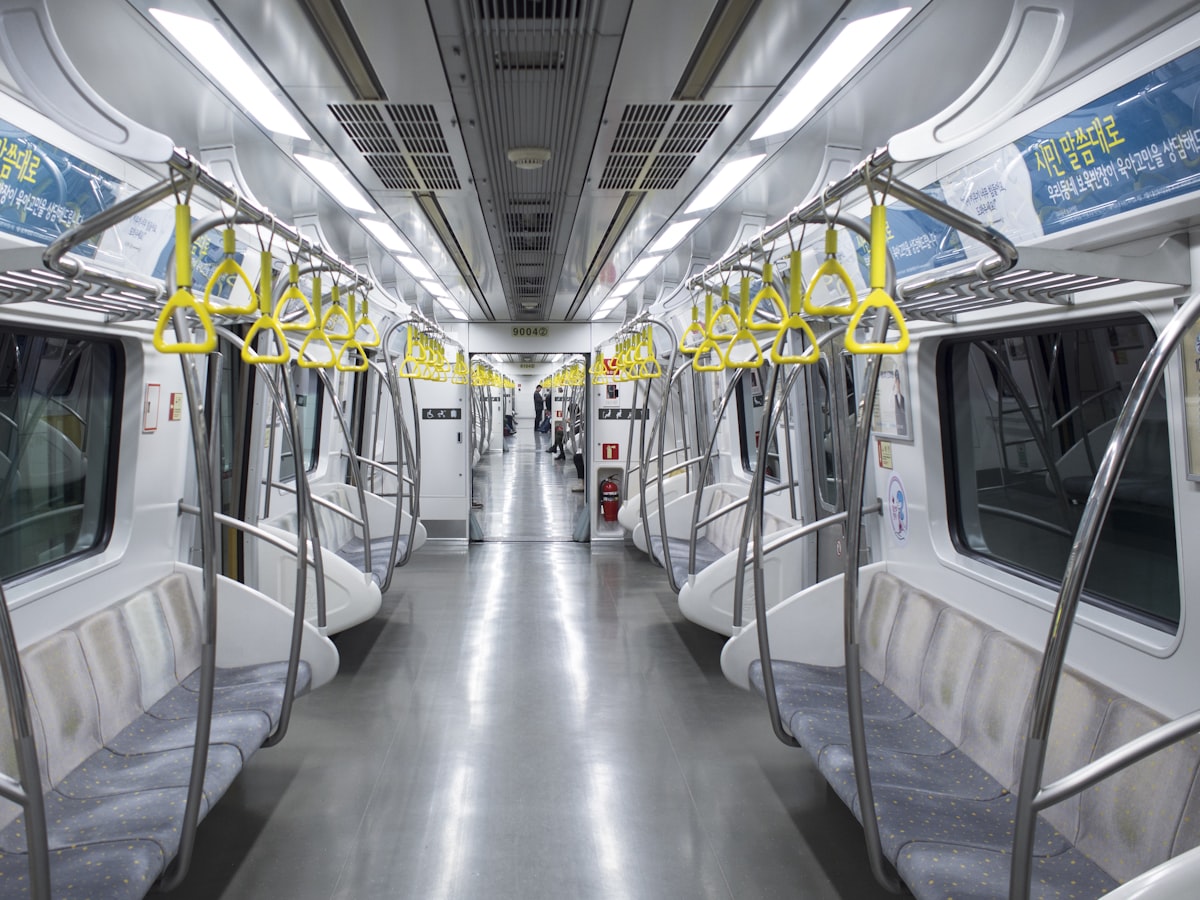 Rows of empty seats and yellow grab handles inside a nearly empty Seoul subway car in the afternoon.