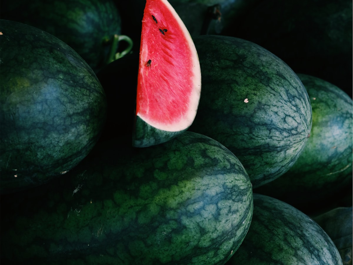 A single cut watermelon wedge set atop a dense pile of whole watermelons