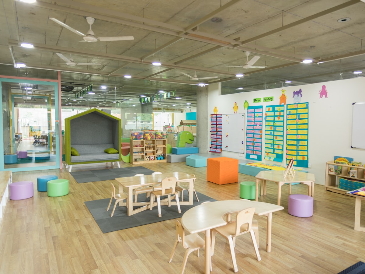 An empty preschool classroom with small children's tables, chairs, and colorful play furniture, no people