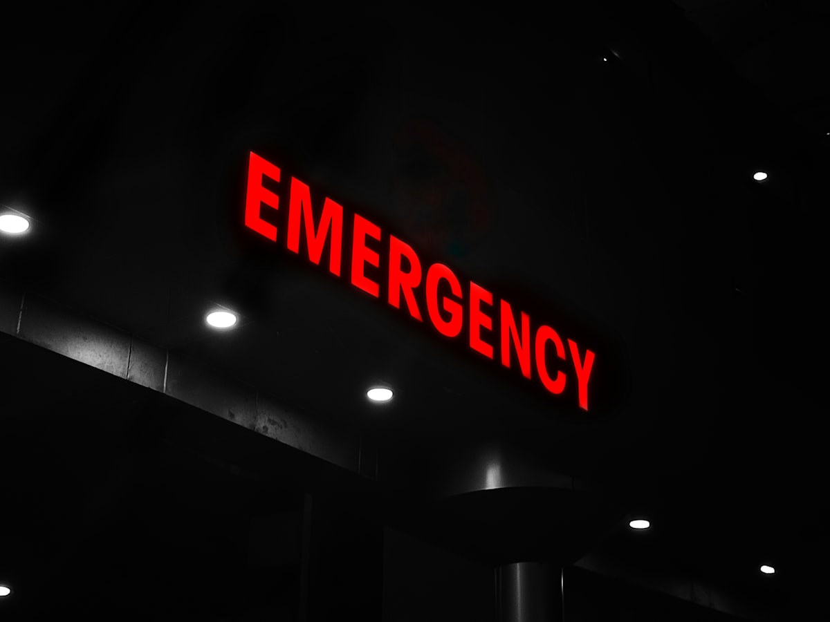 An illuminated red EMERGENCY sign glowing above a dark building entrance at night