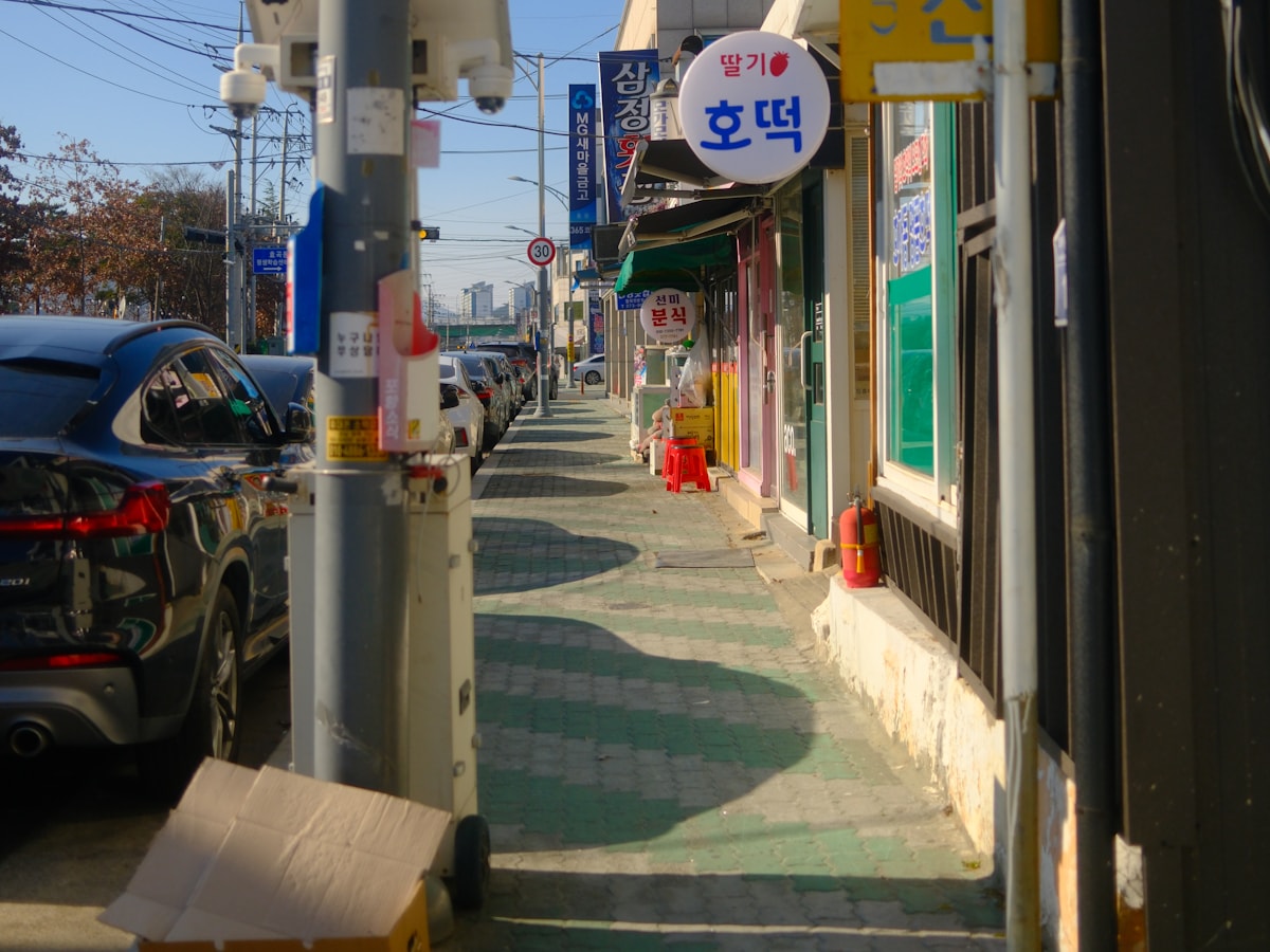 A Korean street lined with small storefronts and hanging signboards, the kind of neighborhood where Uijeongbu's Budae-jjigae Street took shape