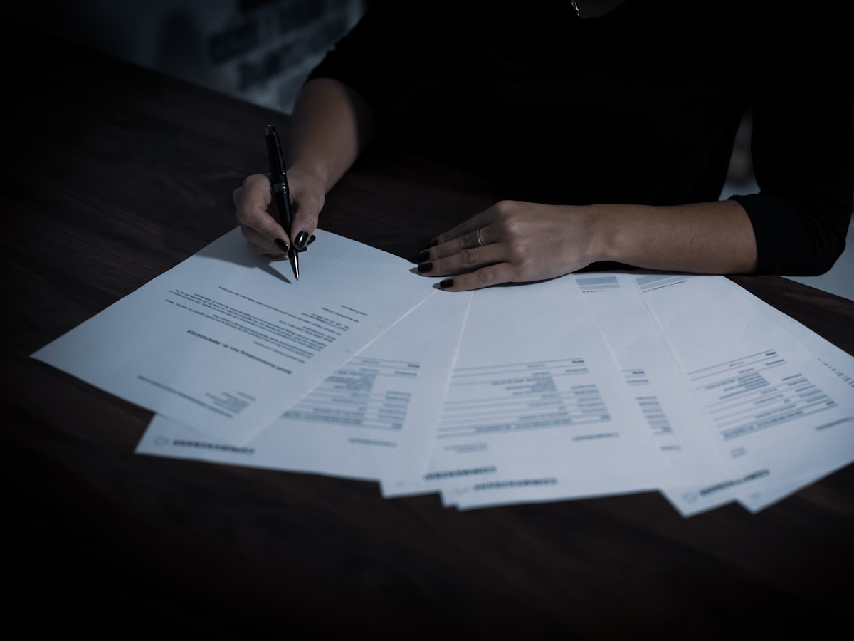 A parent's hands signing a stack of paperwork spread across a desk