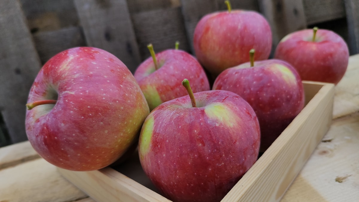 Six red apples in a light wooden crate against weathered boards