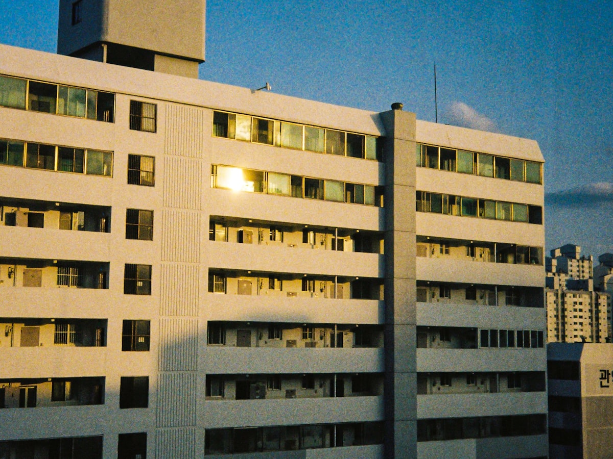 Close-up of a Korean apartment building at dusk, rows of stacked balconies and doors floor above floor, one window lit