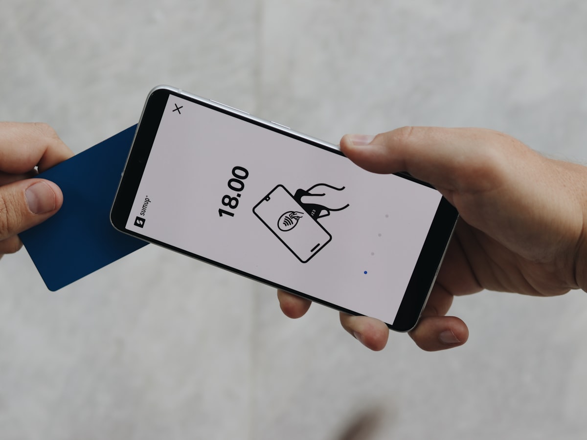 A smartphone displaying an NFC tap icon while a hand holds a card near the screen, illustrating the physical tap motion used to read a chip card