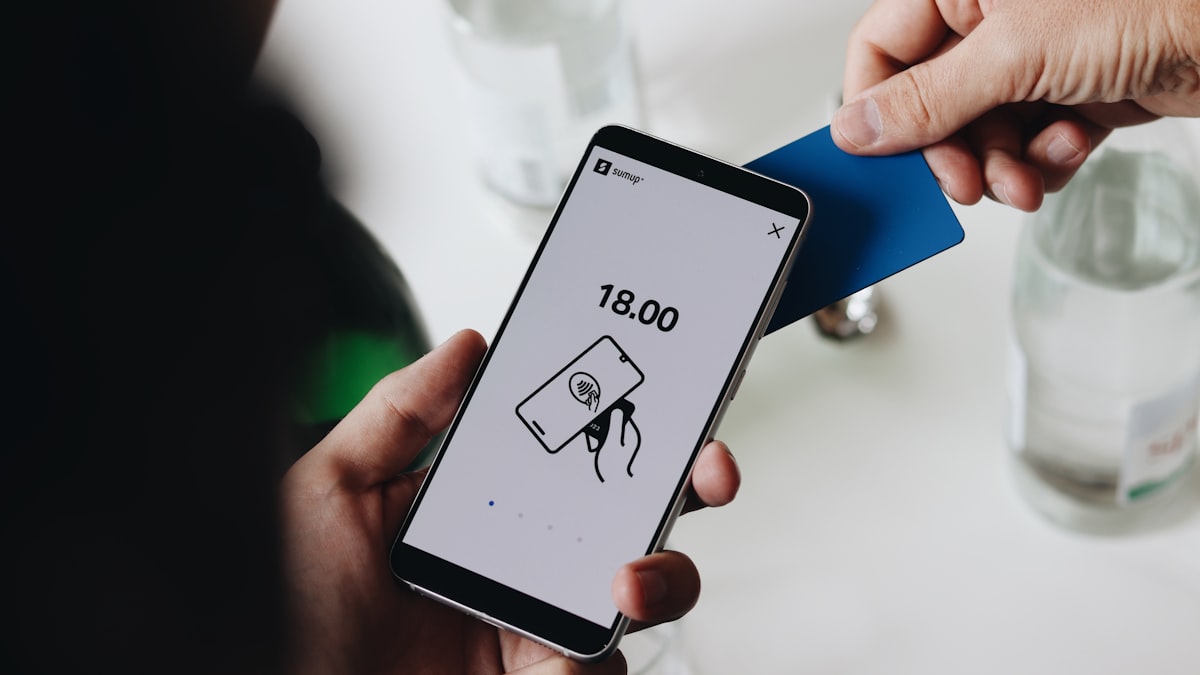 A hand tapping a card near a smartphone screen that shows an NFC tap icon, illustrating the physical tap gesture behind Korea's Mobile Residence Card activation