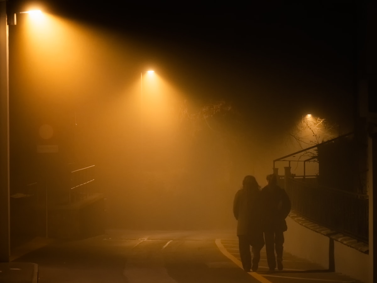 Warm streetlight beams cutting through fog on a quiet street at night, evoking the glow and haze of an old neighborhood fogging truck