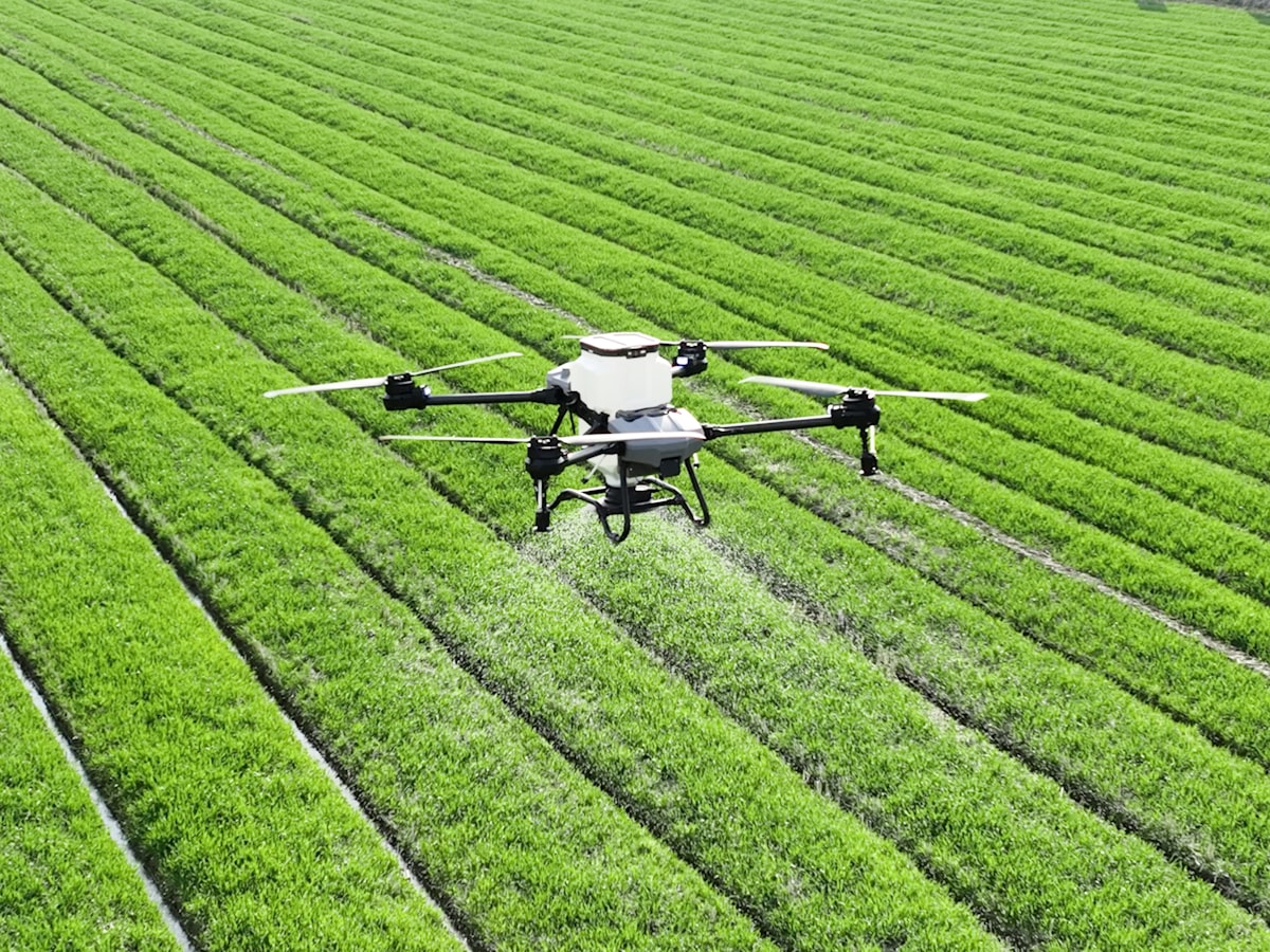 An agricultural spray drone hovering low over green rows of vegetation, releasing a fine mist -- the kind of precision drone technology Seoul districts now use for mosquito and pest control