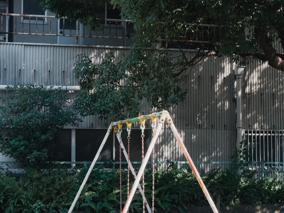 Weathered swing-set frame with rust on the chains and posts at an older apartment-complex playground