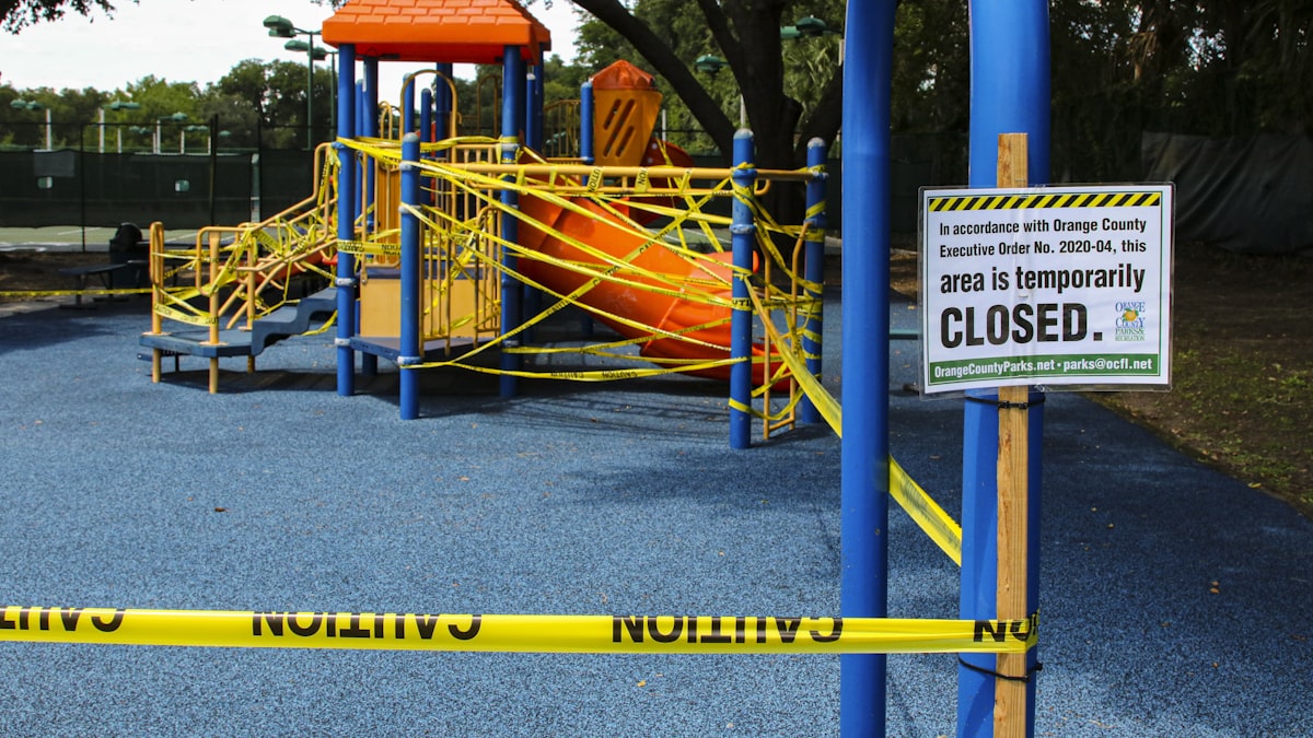 Playground climbing frame and slide wrapped in yellow caution tape beside a temporarily closed sign