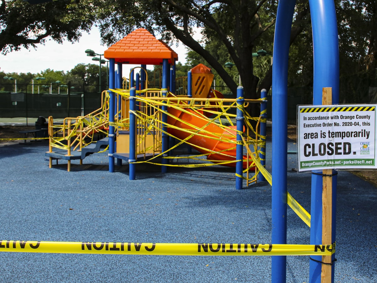 Playground jungle gym and slide wrapped in yellow caution tape with a temporary closure sign, outdoor recreation area