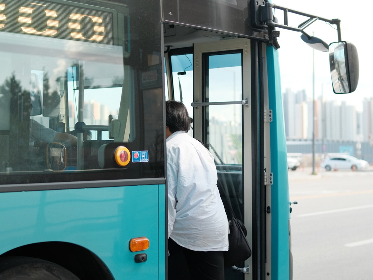 A commuter boarding a city bus through the front door in Chuncheon, South Korea, seen from outside near the driver's side mirror