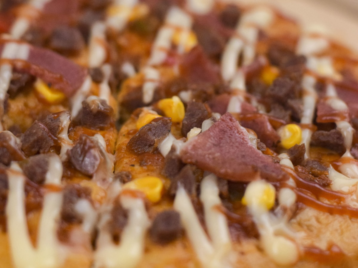 Close-up of a Korean-style pizza topped with corn kernels, chunks of meat, and a drizzled mayo-based sauce