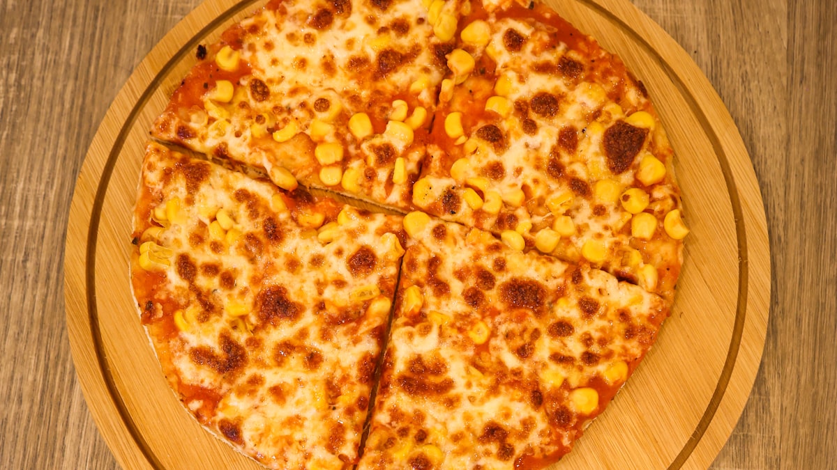 Korean-style pizza topped with sweet corn and melted cheese, sliced on a round wooden board