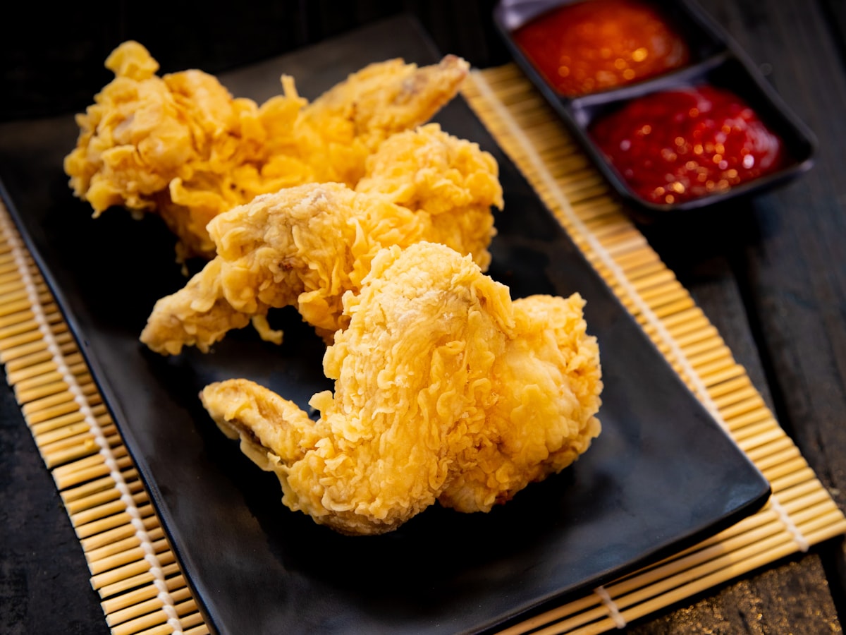 A plate of Korean-style fried chicken wings with two dipping sauces, served on a black plate over a bamboo table mat
