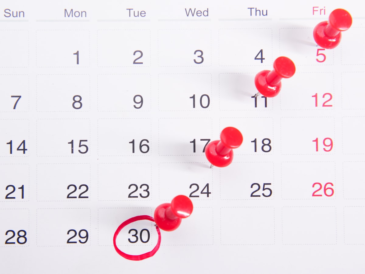 A wall calendar with the 30th circled in red marker, and a diagonal trail of red pushpins marking earlier dates in the same week