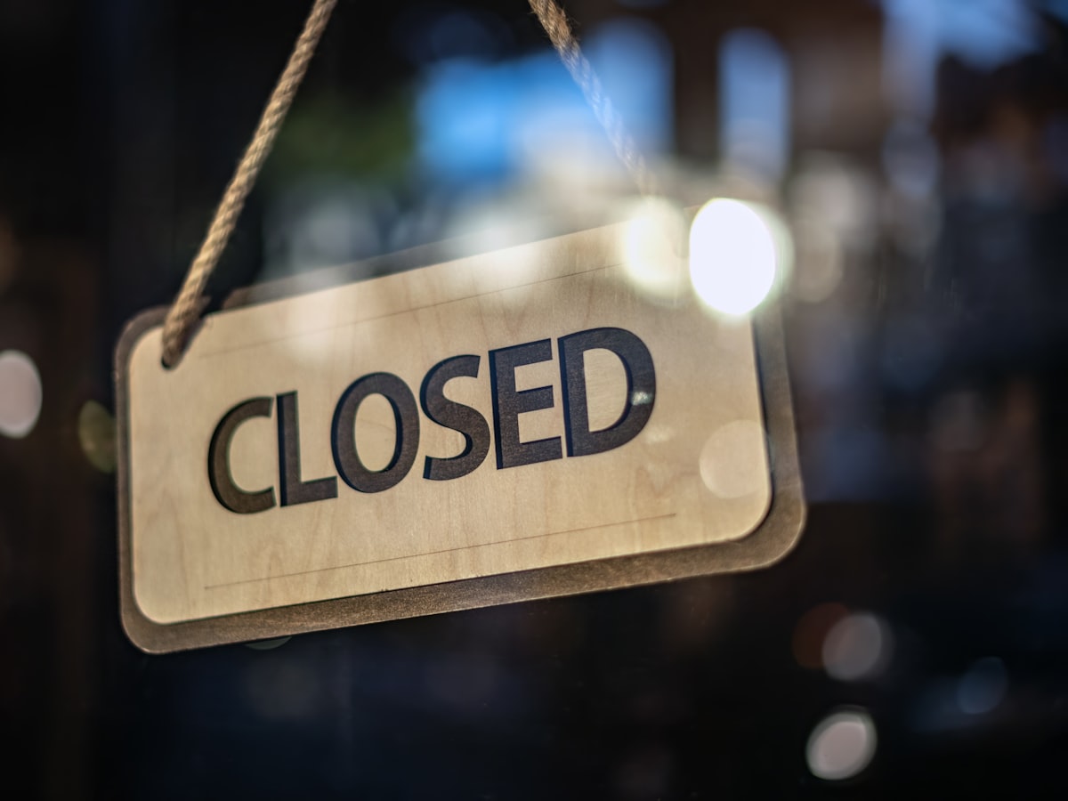 A wooden 'Closed' sign hanging on a glass storefront door