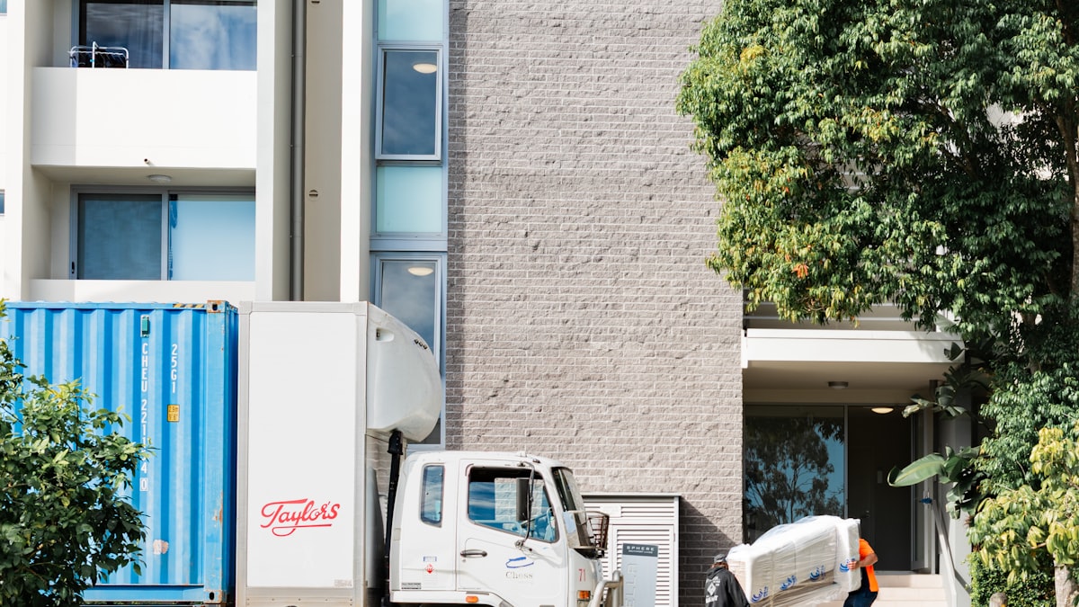 Moving truck and shipping container at an apartment entrance as a worker carries wrapped furniture