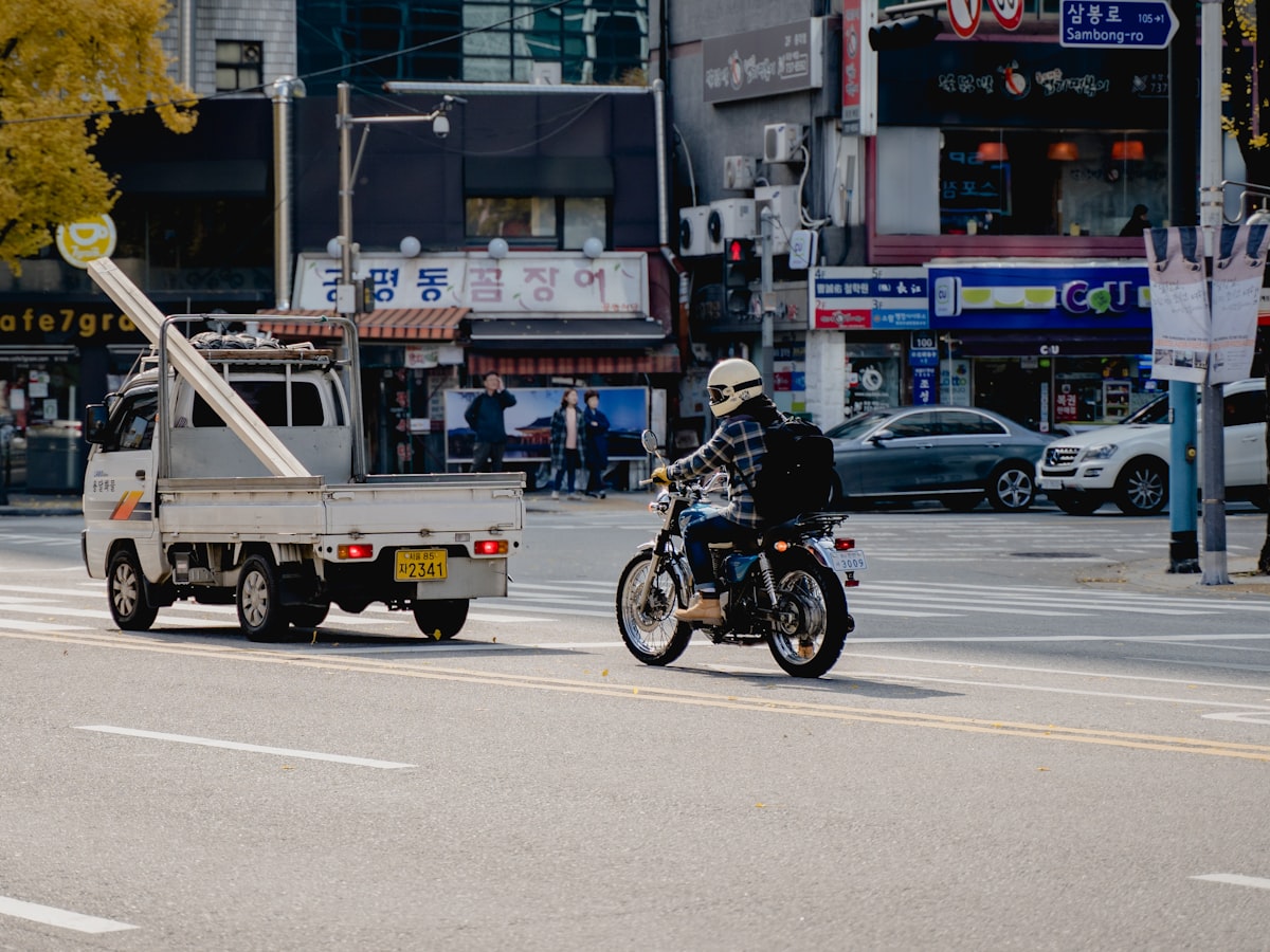 A motorcyclist rides through a Seoul intersection on Sambong-ro, past storefronts with Korean-language signage and a small delivery truck