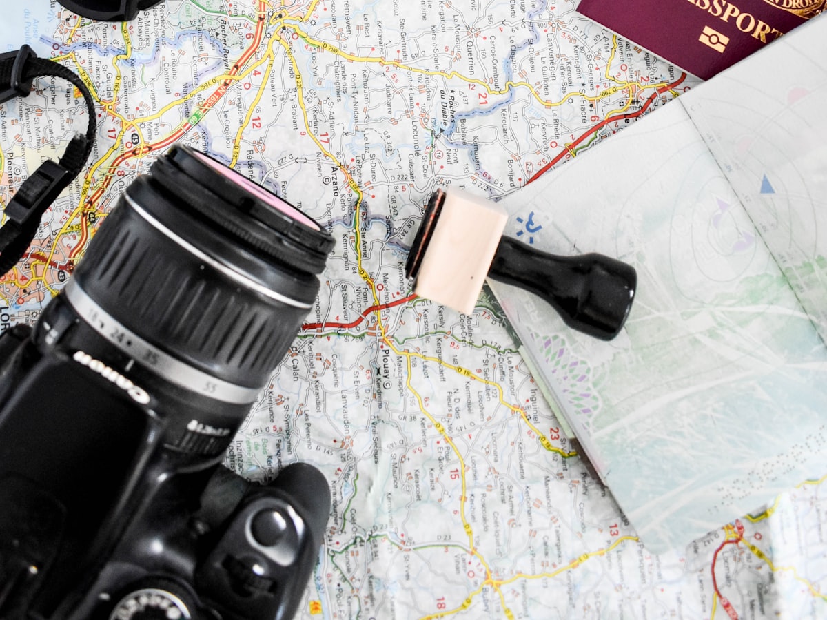 A passport, a camera, and a stamp resting on top of an open paper travel map