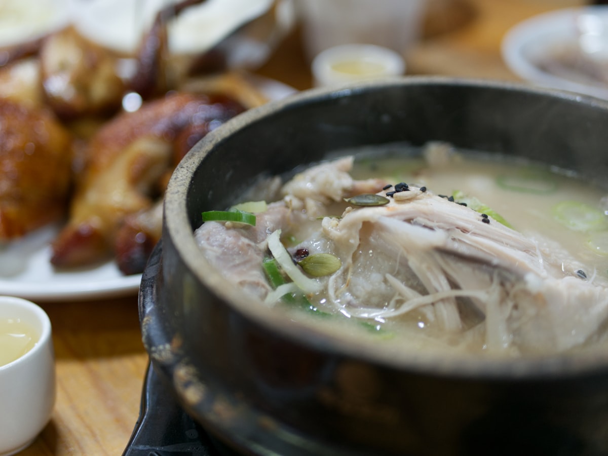 Samgyetang, Korean ginseng chicken soup, served bubbling in a black stone pot topped with scallions and pine nuts
