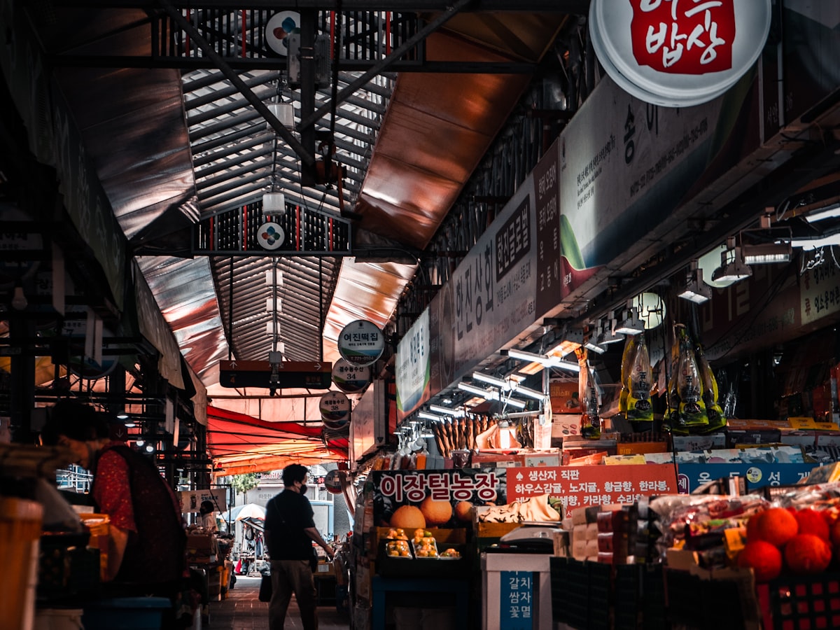 A covered traditional Korean market alley in Jeju-si lined with produce stalls and shop signs