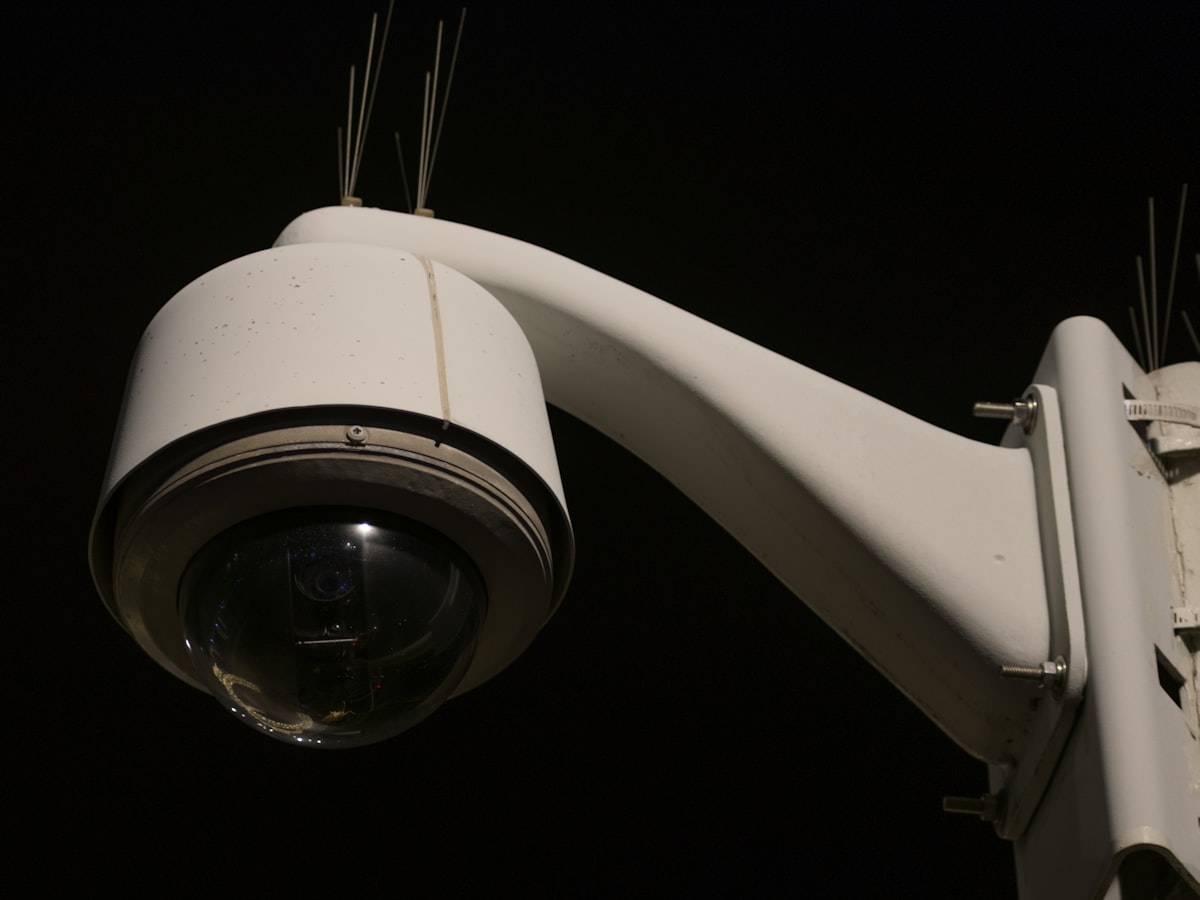 A dome-style surveillance camera mounted on an arm at night, its lens visible against a dark background