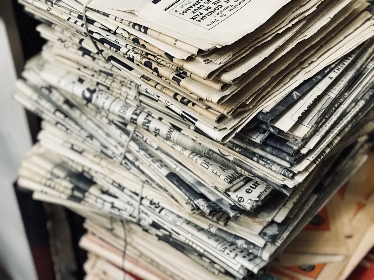 A thick, string-tied bundle of old, yellowed newspapers stacked on a shelf