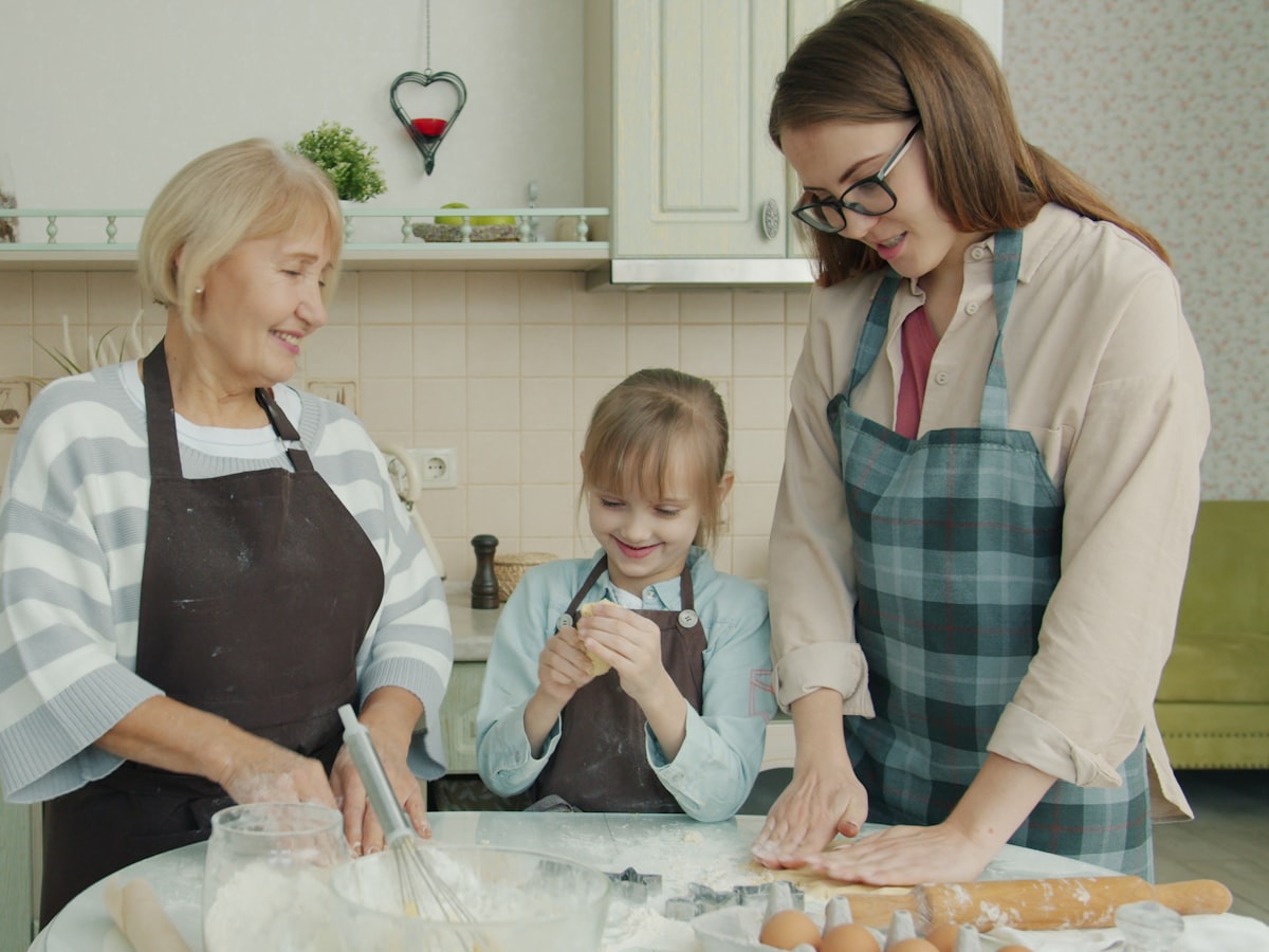 Three generations of one family — a grandmother, mother, and child — smiling together while baking in a home kitchen