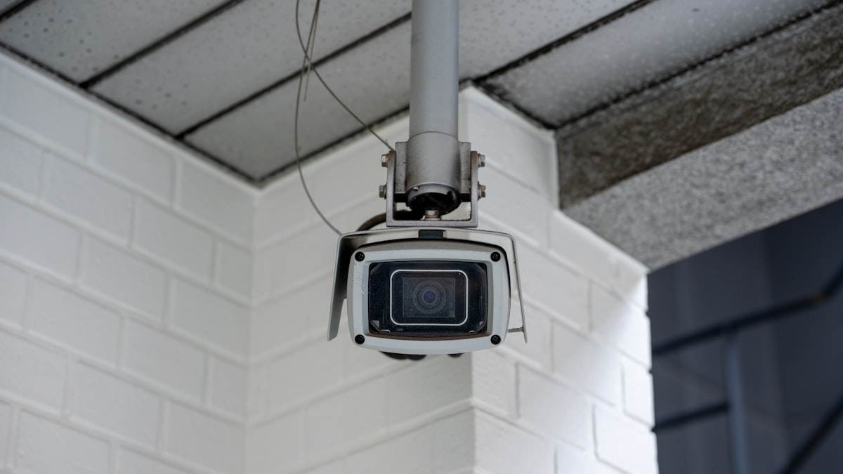 Boxy white security camera mounted on a bracket against a white brick building corner