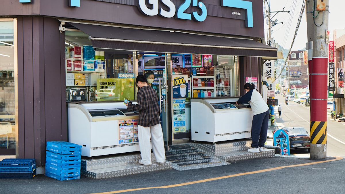 Two customers browse open freezer chests outside a GS25 convenience store on a Korean street