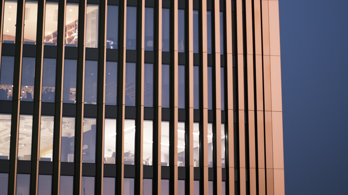 Office tower facade at dusk with a few floors still lit behind vertical fins