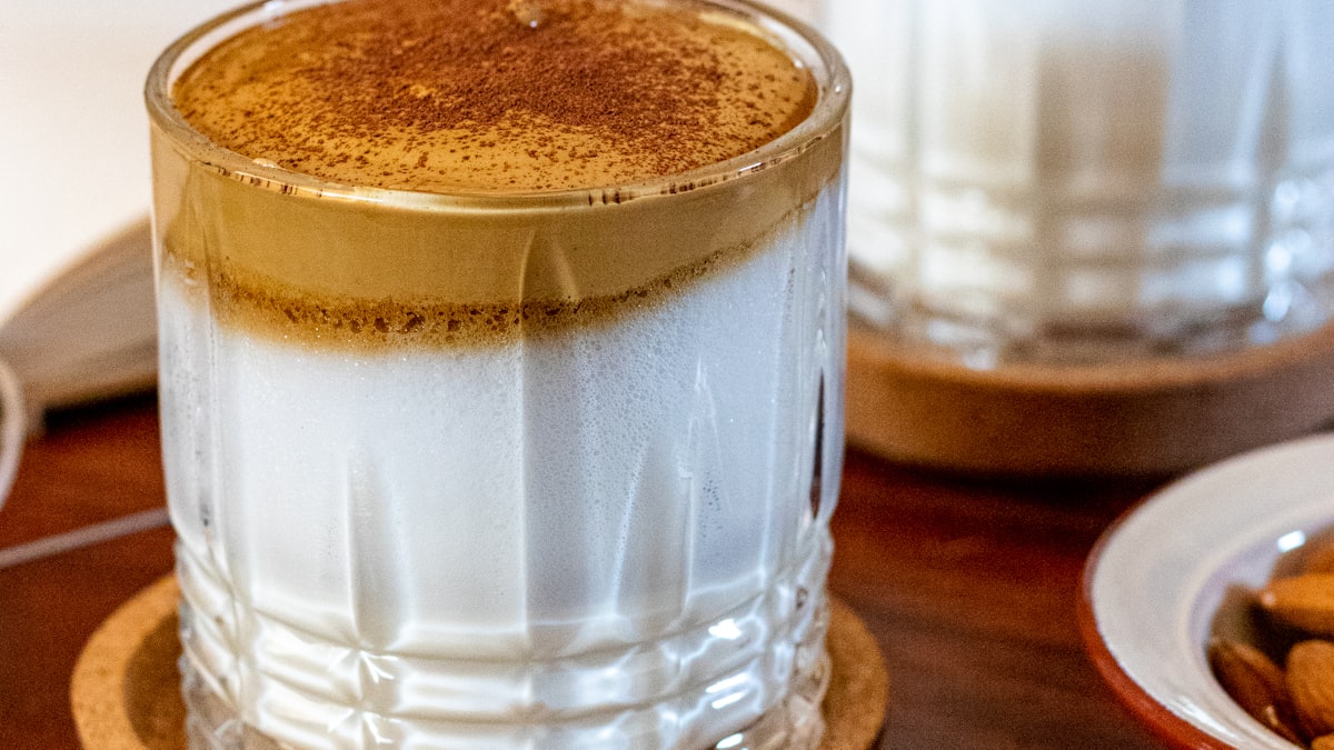 Glass of dalgona coffee: whipped tan coffee foam dusted with cocoa over cold milk