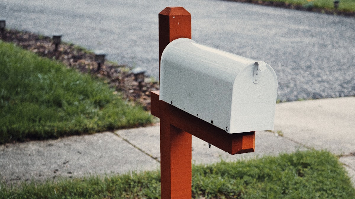 White curbside mailbox on a red wooden post beside a suburban road
