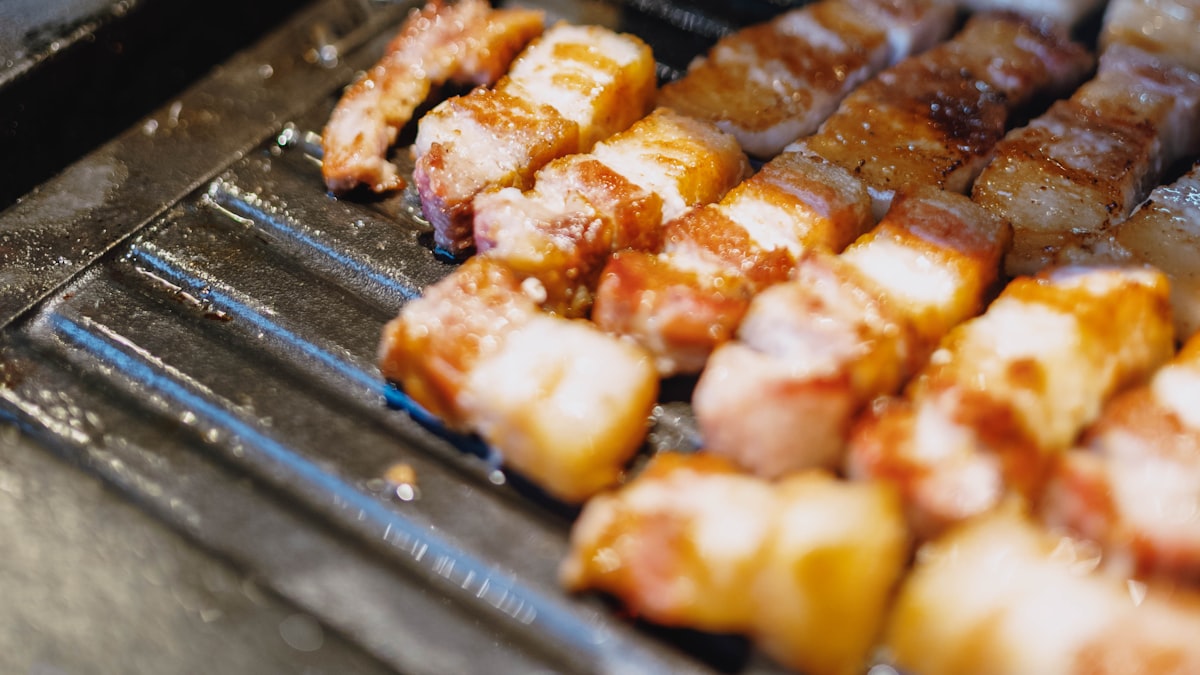 Close-up of Korean pork belly (samgyeopsal) strips sizzling on a metal BBQ grill